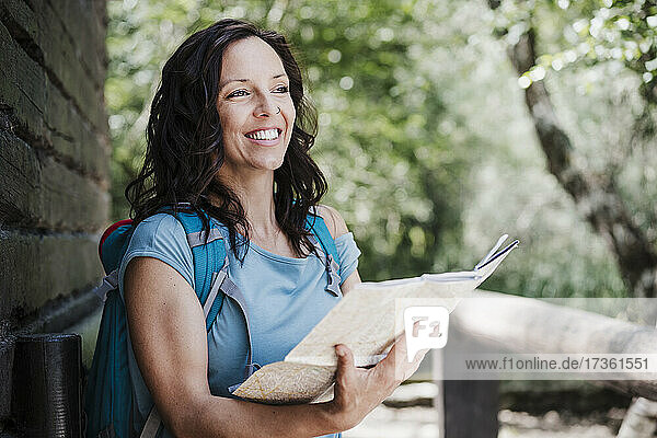 Lächelnde Touristin schaut weg  während sie eine Karte im Wald hält