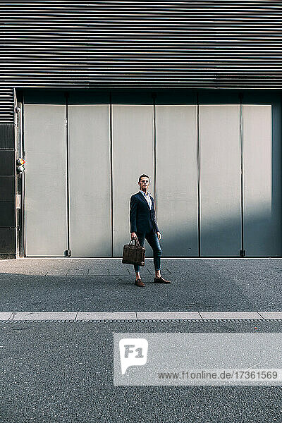 Businessman holding briefcase while standing on footpath