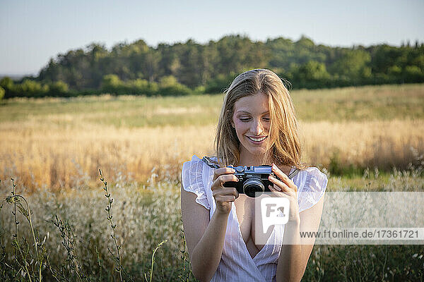 Lächelnde junge Frau schaut in die Kamera  während sie auf einem Feld steht