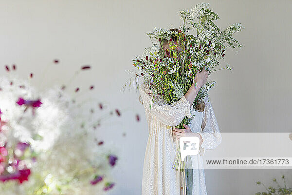 Covered face of woman with wild flowers bouquet in studio