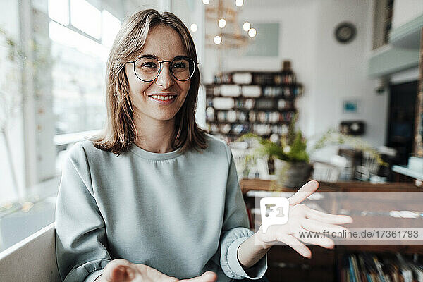 Lächelnde junge Frau mit Brille  die in einem Café sitzt und gestikuliert