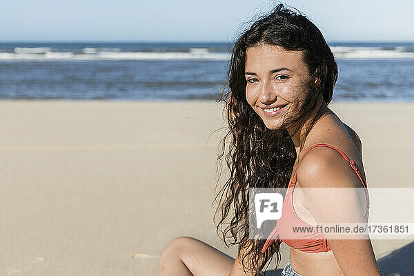Lächelnde junge Frau am Strand sitzend im Urlaub