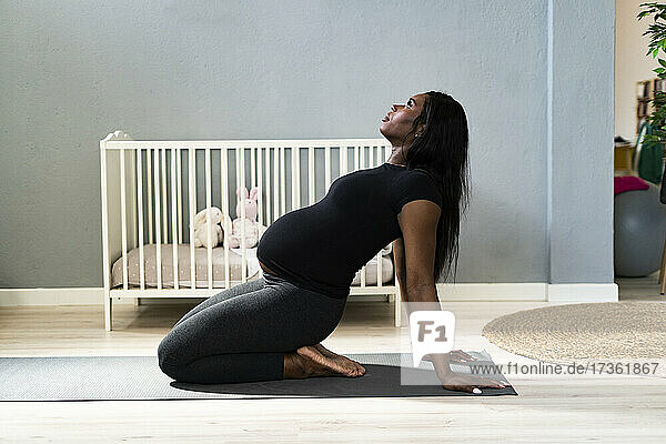 Schwangere junge Frau lehnt sich zurück  während sie zu Hause Yoga übt