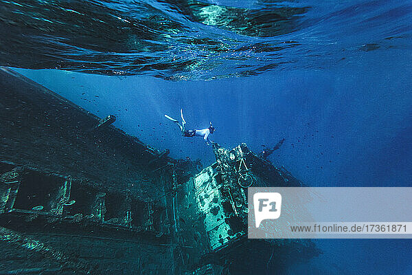 Mann schwimmt unter Wasser in der Nähe eines verlassenen Schiffes im Meer