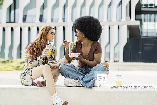Female friends enjoying food while sitting on bench