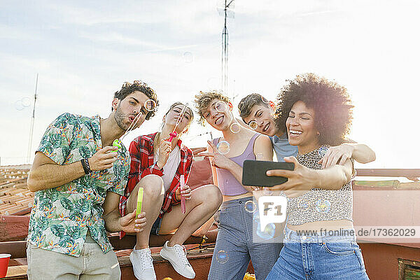 Fröhliche multiethnische Freunde machen ein Selfie beim Spielen mit Seifenblasen auf der Terrasse