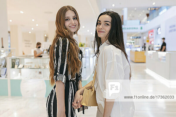 Female friends holding hands while standing at shopping mall