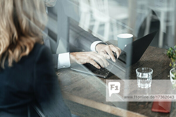 Männlicher Berufstätiger tippt auf einem Laptop  während er mit einer Geschäftsfrau in einem Café sitzt