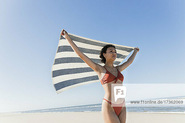 Junge Frau winkt mit Handtuch am Strand im Urlaub
