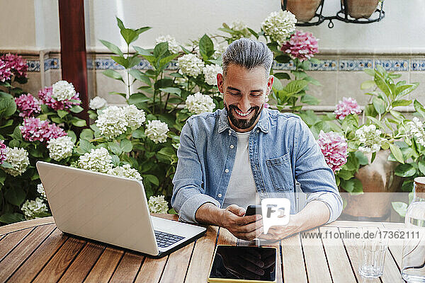 Lächelnder Geschäftsmann  der ein Smartphone im Hinterhof benutzt