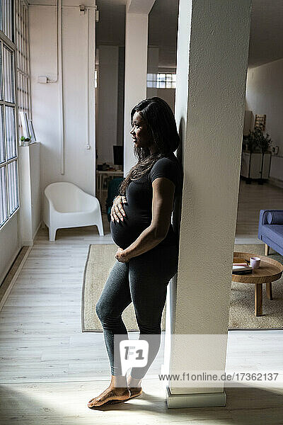 Pregnant woman leaning against column at home