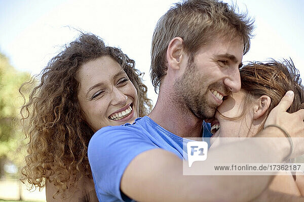 Glückliche Frau mit lockigen Haaren betrachtet ein junges Paar  das sich im Park umarmt