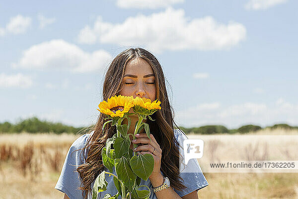 Junge Frau riecht an Sonnenblumen an einem sonnigen Tag