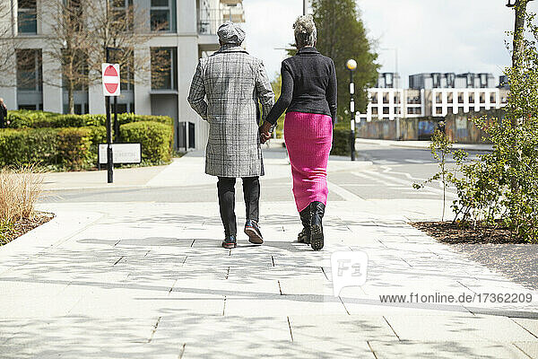 Paar hält sich an den Händen  während es an einem sonnigen Tag auf einem Fußweg spazieren geht