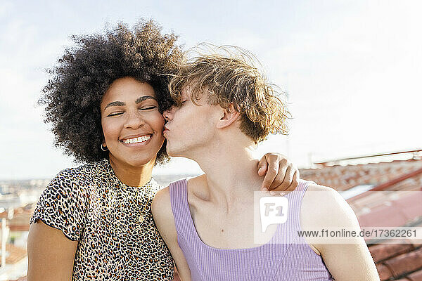 Young male kissing Afro female friend on cheek at rooftop during party