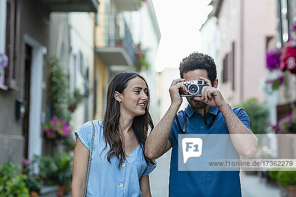 Woman looking at boyfriend photographing through camera in town