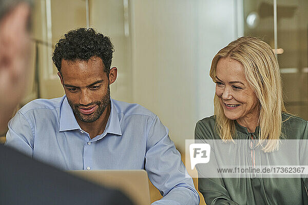 Geschäftsfrau schaut auf einen Laptop  während sie neben einem männlichen Kollegen im Sitzungssaal sitzt