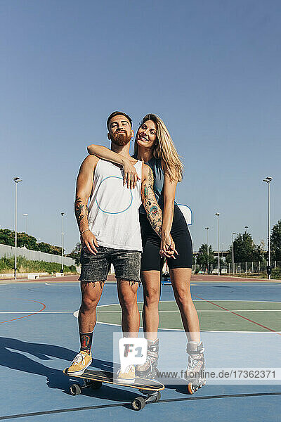 Lächelndes junges Paar hält sich am Basketballplatz an einem sonnigen Tag an den Händen