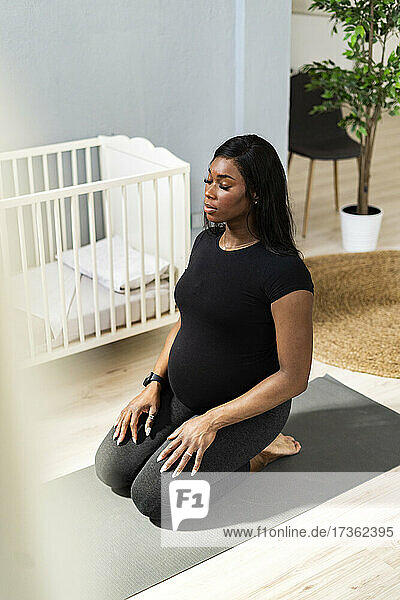 Junge schwangere Frau mit geschlossenen Augen übt Yoga auf der Matte zu Hause