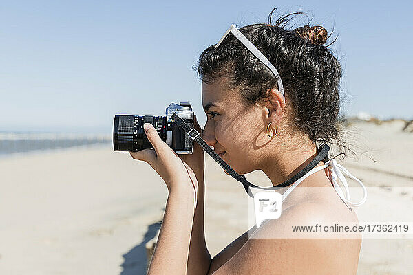 Woman photographing through camera at beach on sunny day