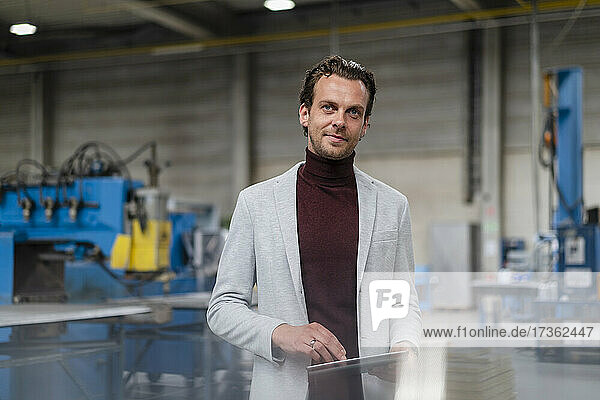 Businessman in gray blazer standing with digital tablet in factory