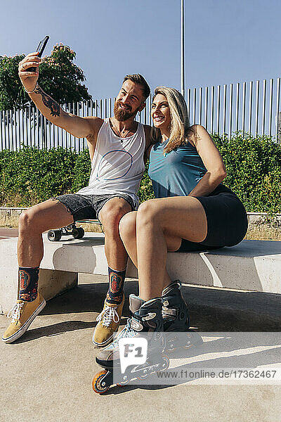 Glücklicher junger Mann  der ein Selfie mit seiner Freundin macht  während er auf einer Bank sitzt