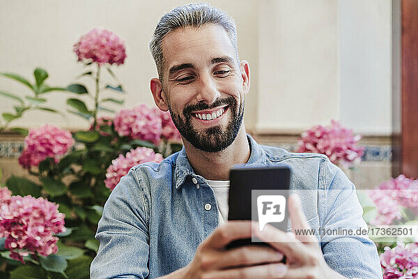 Mittlerer erwachsener Geschäftsmann  der lächelt  während er ein Smartphone im Hinterhof benutzt