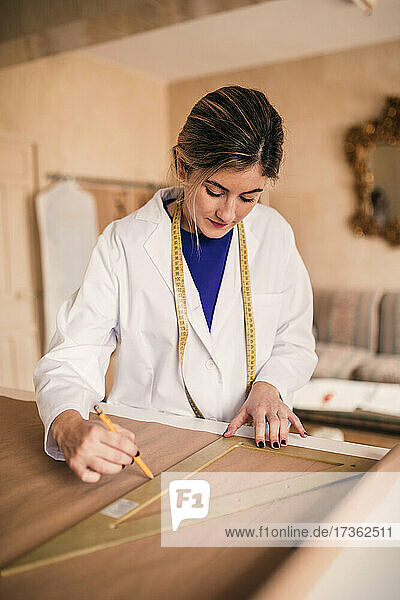 Female tailor using ruler while measuring fabric on workbench
