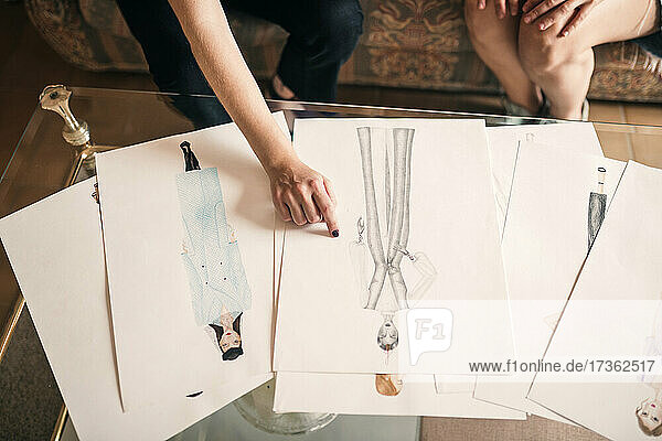 Weibliche Modeexpertin zeigt auf eine Skizze  während sie mit einem Kunden spricht