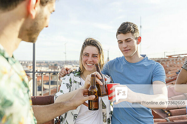 Männliche und weibliche Freunde stoßen mit Getränken auf der Terrasse während einer Wochenendparty an