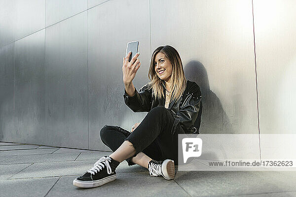 Frau  die ein Selfie mit ihrem Smartphone vor einer Metallwand macht