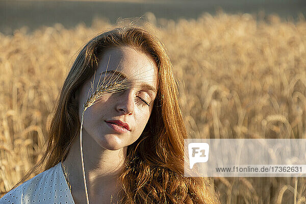 Woman with wheat on closed eyes during sunny day