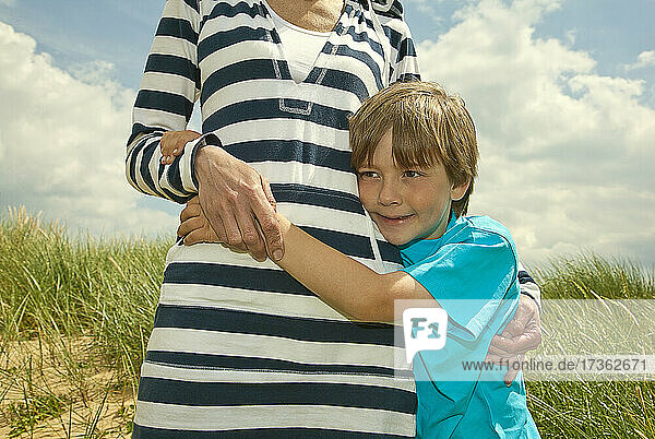 Sohn umarmt Mutter am Strand stehend