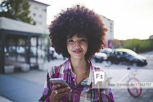 Porträt einer selbstbewussten jungen Frau mit Afrofrisur in der Stadt in der Abenddämmerung