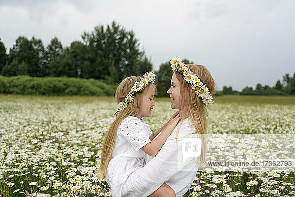 Smiling mother carrying daughter at chamomile field