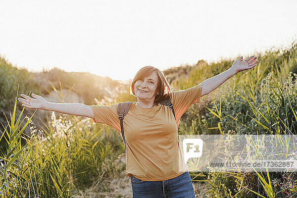 Happy woman with arms outstretched standing on trail near grass