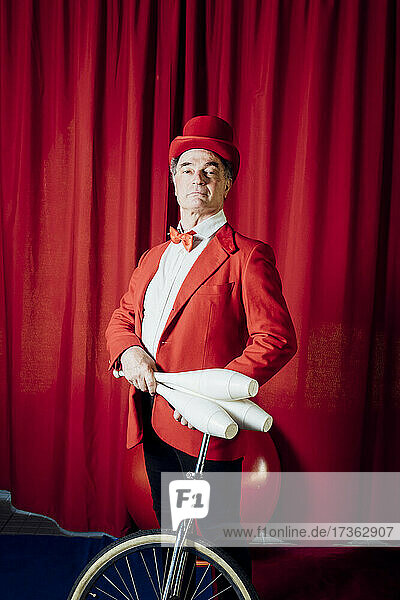 Zirkusartist hält Jonglierstifte  während er mit dem Einrad im Zirkus steht