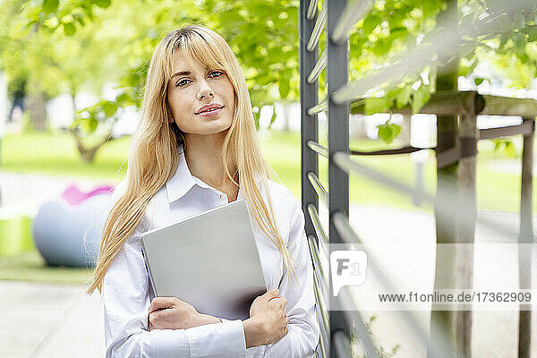 Junge blonde Geschäftsfrau hält Laptop an Metall im Büropark