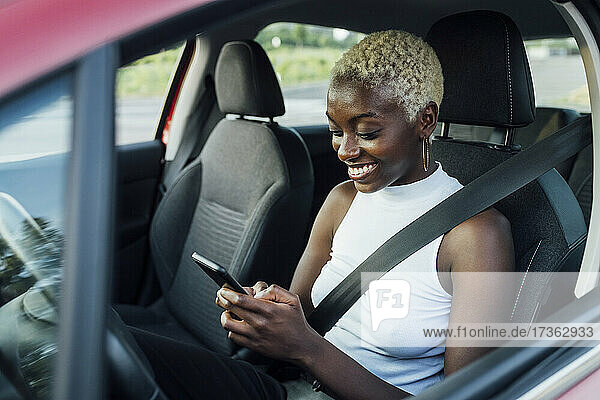 Lächelnde Frau  die ein Mobiltelefon benutzt  während sie im Auto sitzt