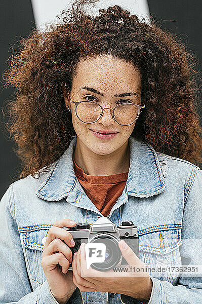 Confident young curly haired woman holding camera