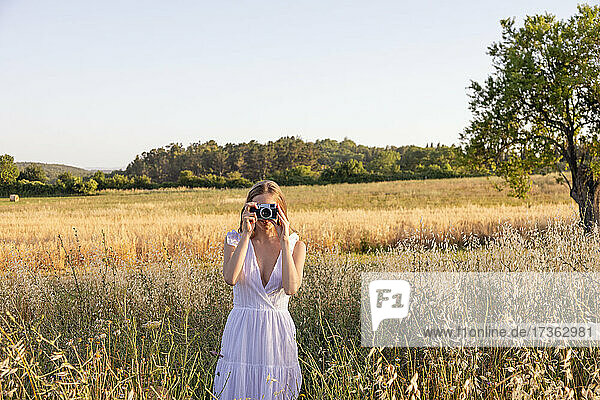 Young woman photographing through camera in field