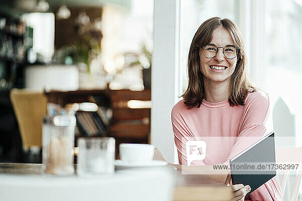 Glückliche junge Geschäftsfrau sitzt mit digitalem Tablet in einem Cafe