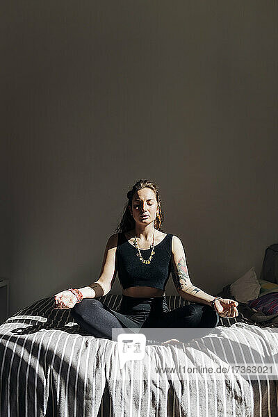 Frau übt Yoga im Schneidersitz auf dem Bett in einer Wohnung