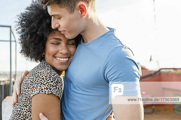 Lächelnde junge Frau umarmt ihren Freund auf der Terrasse