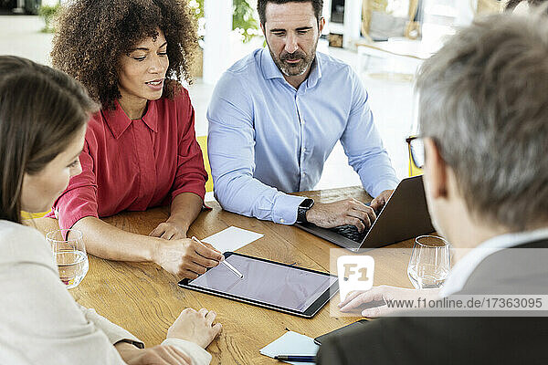 Female professional using digital tablet while discussing with colleague at office
