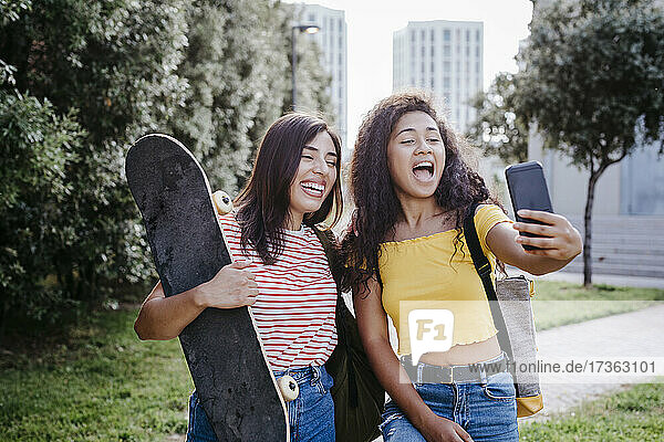 Junge Frau nimmt Selfie durch Smartphone mit weiblichen Freund hält Skateboard im Park