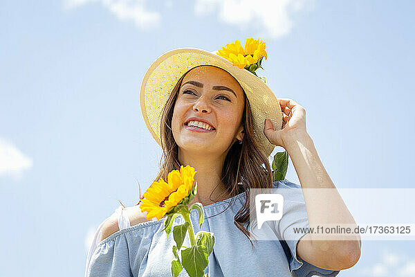 Glückliche Frau mit Hut und Sonnenblumen an einem sonnigen Tag