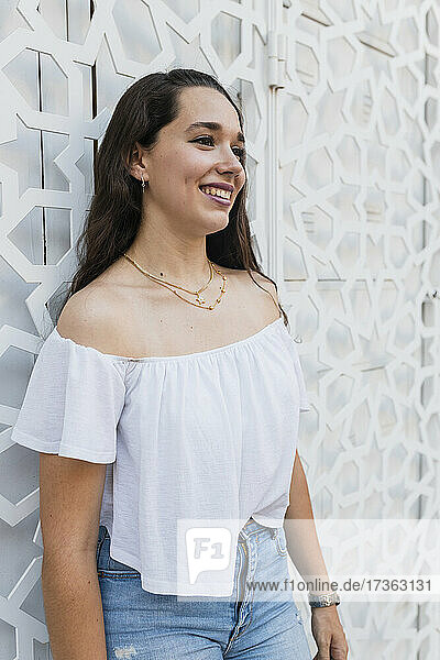 Lächelnde schöne junge Frau vor einer Wand stehend
