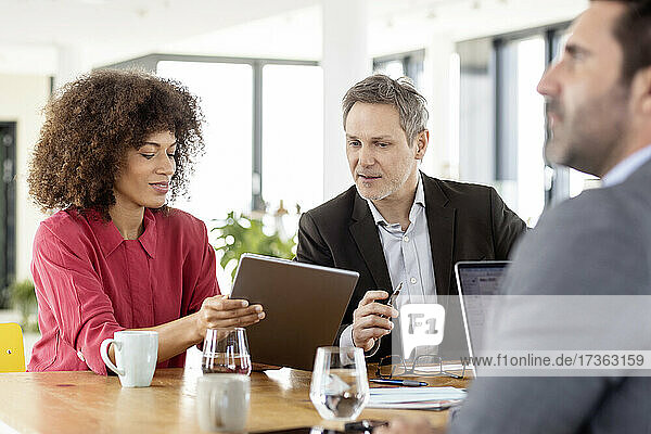 Colleagues with digital tablet discussing while working in meeting