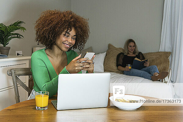 Lächelnde Afro-Geschäftsfrau  die ein Smartphone am Schreibtisch im Home-Office benutzt